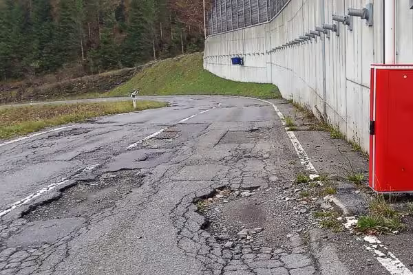 Schranke neben einer Fahrbahn mit schadhaftem Asphaltbelag